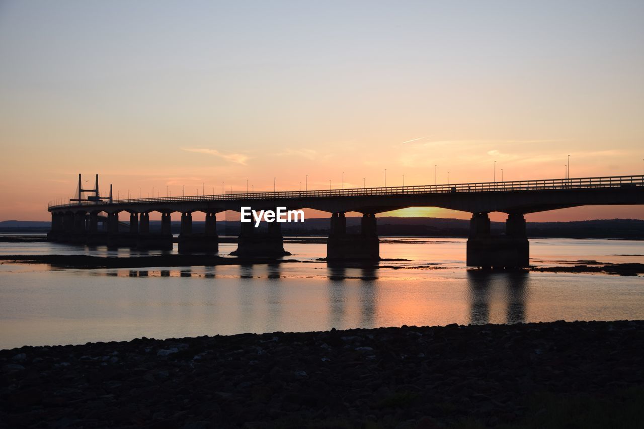 BRIDGE OVER RIVER AGAINST ORANGE SKY