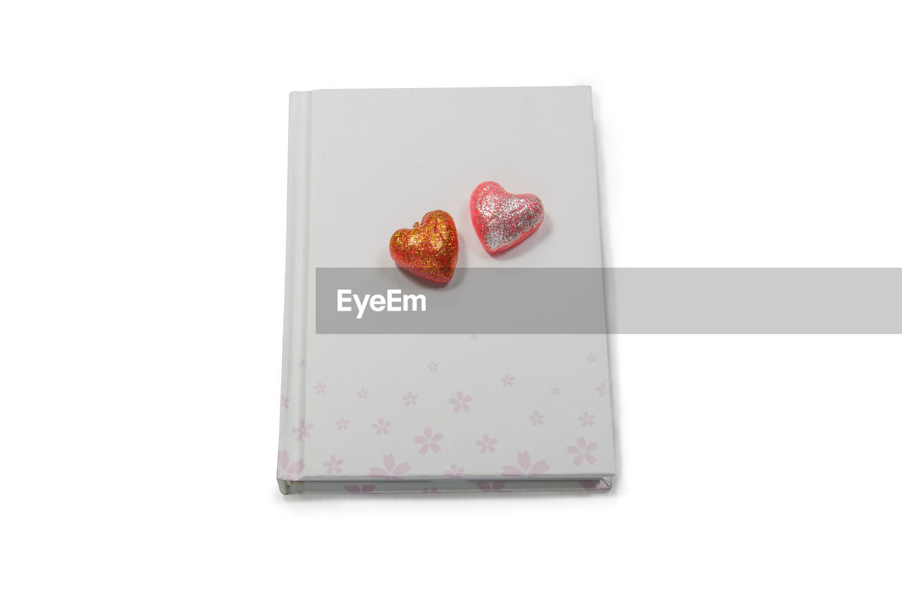 Close-up of heart shape decorations on diary over white background