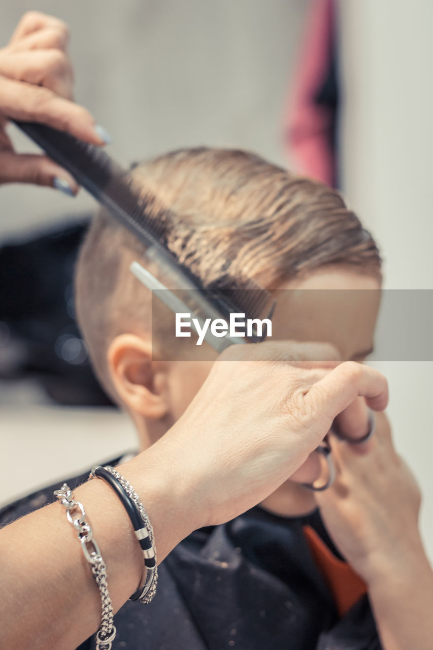 Cropped hands of female barber cutting boy hair in salon