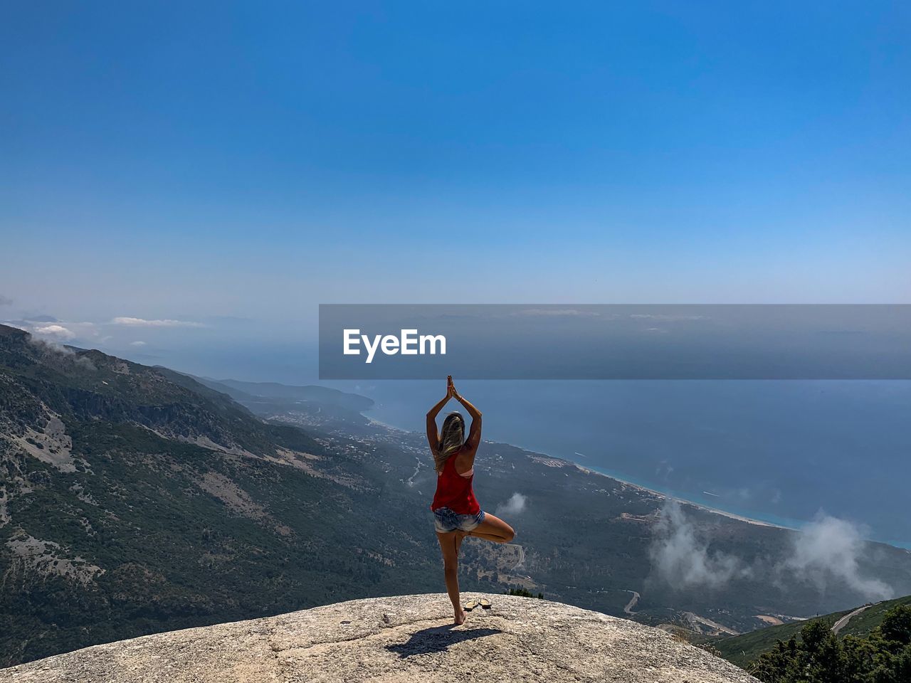 Rear view of woman standing on one leg over mountain against sky