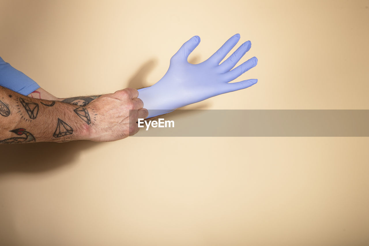 Cropped hands of person putting on surgical gloves against light background person