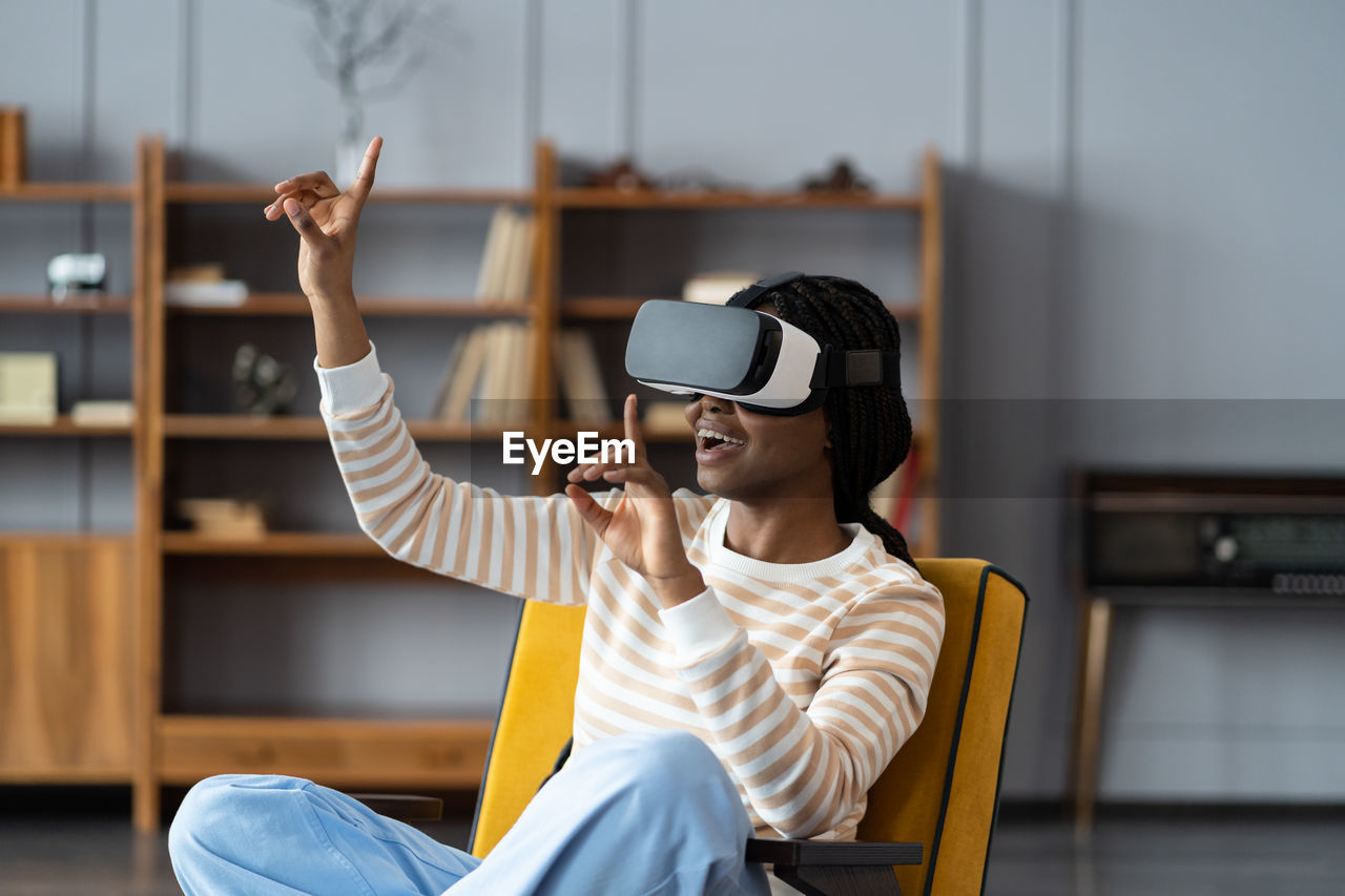 Excited african woman leaning on chair wearing vr headset playing in virtual games during work break