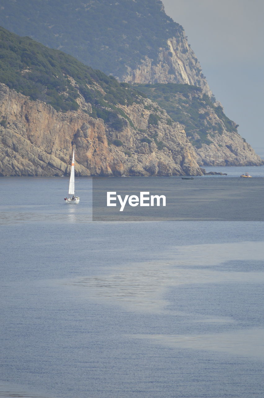 SAILBOAT SAILING ON SEA AGAINST MOUNTAINS