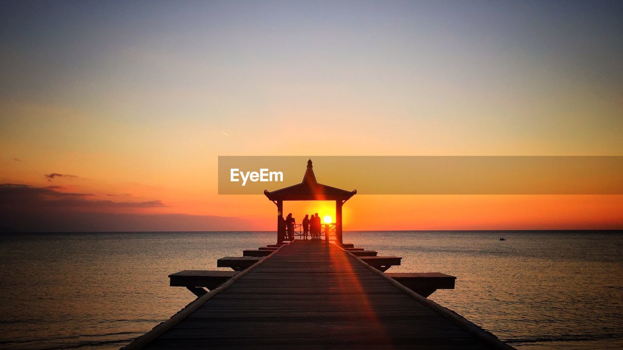 Silhouette people on gazebo by sea against sky during sunset