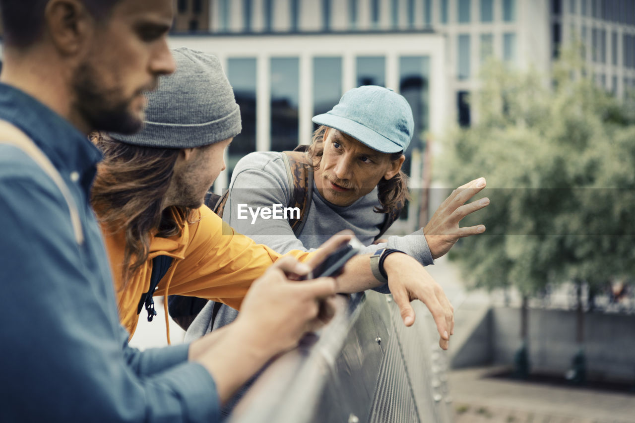 Male friends talking with each other while leaning on retaining wall