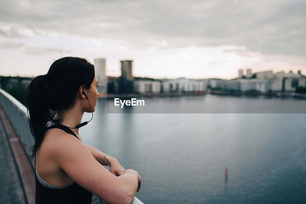 Side view of female athlete looking at city while standing on footbridge over sea