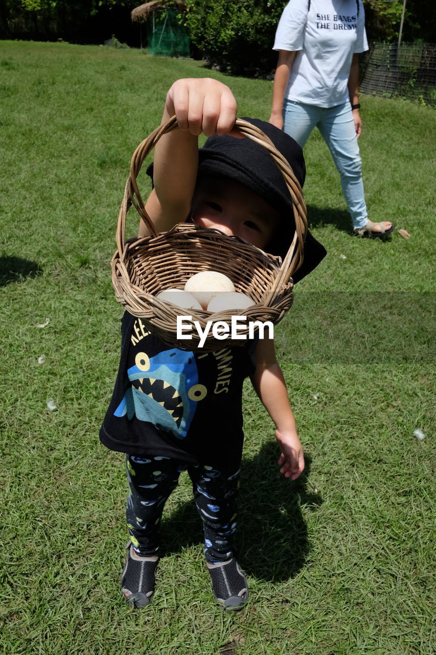 Boy holding eggs in basket while standing on field