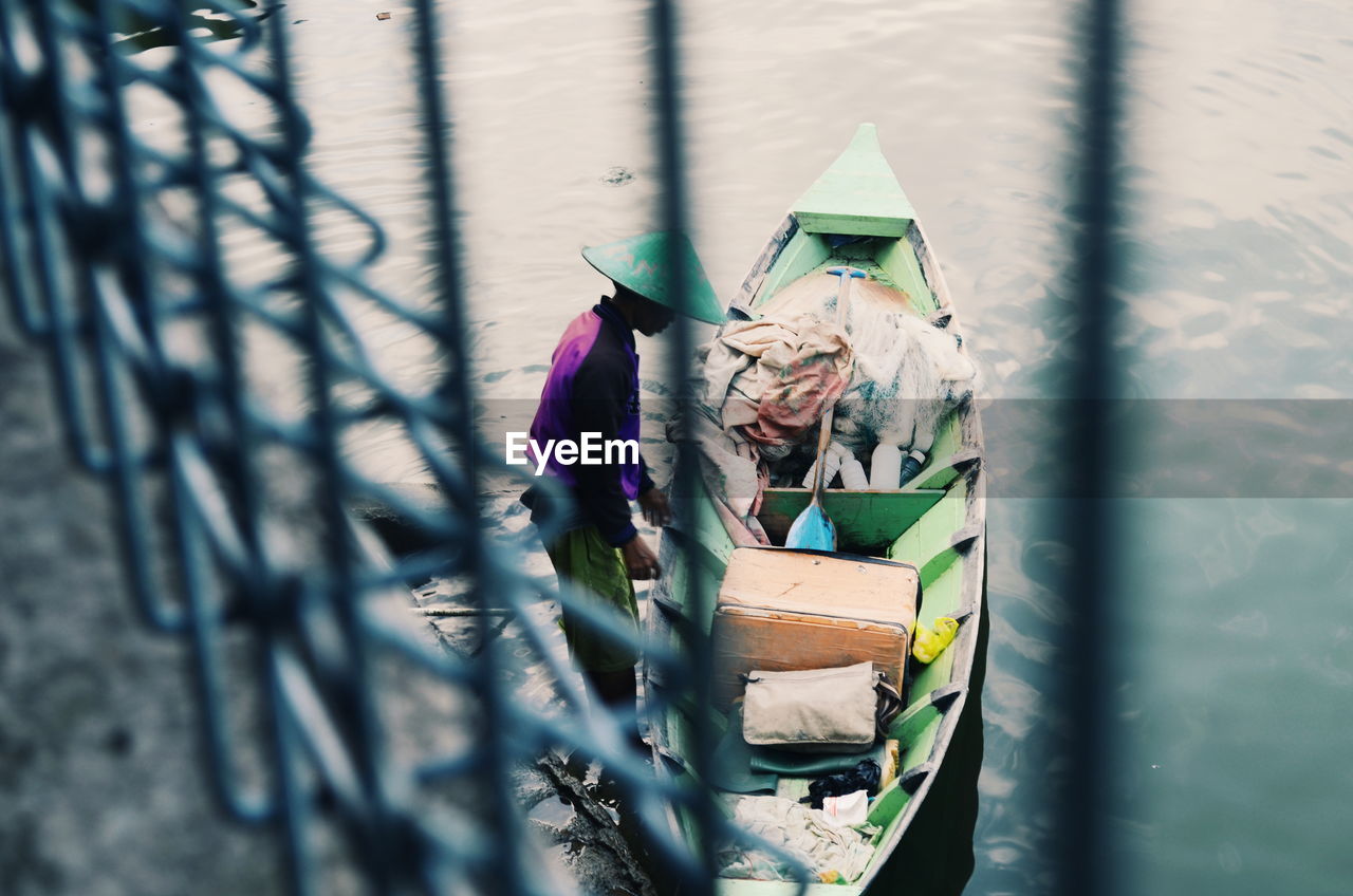 Man by boat on lake seen through fence