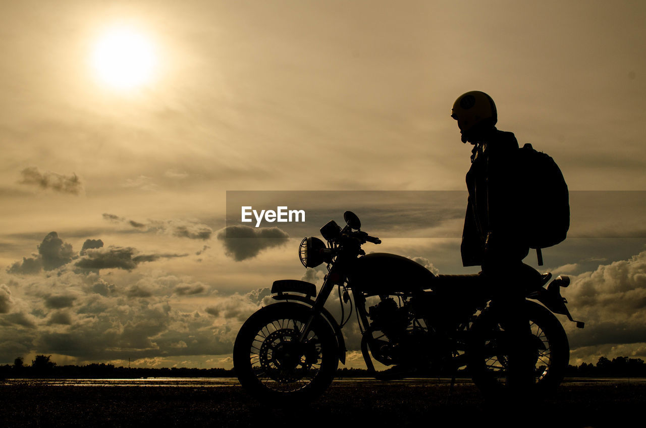 Silhouette man standing by motorcycle against sky during sunset