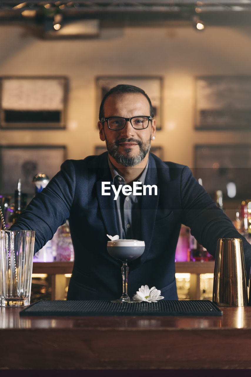 Portrait of smiling bartender standing at counter in bar