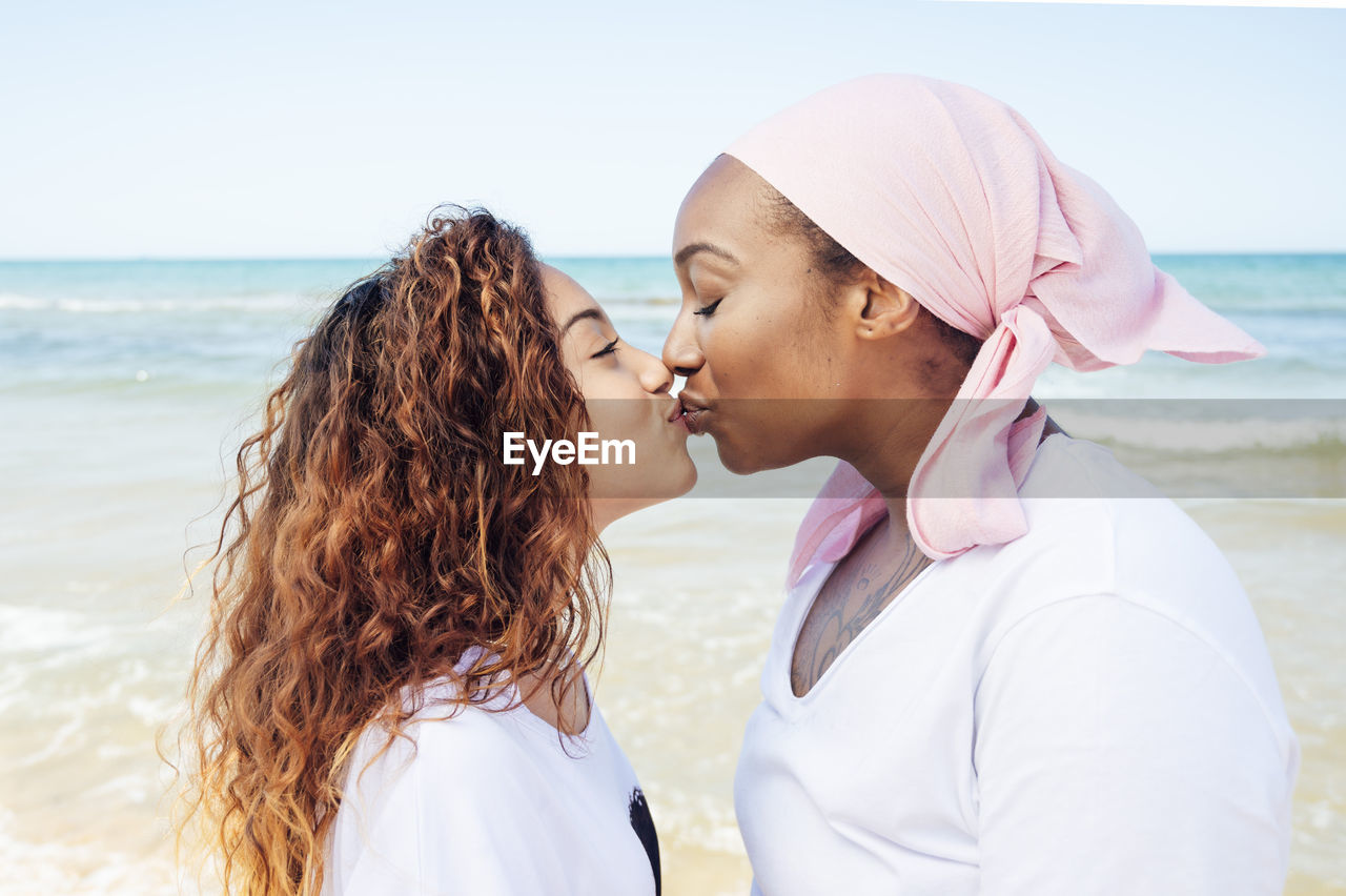 Side view of content african american adult mother and young daughter standing on beach near sea