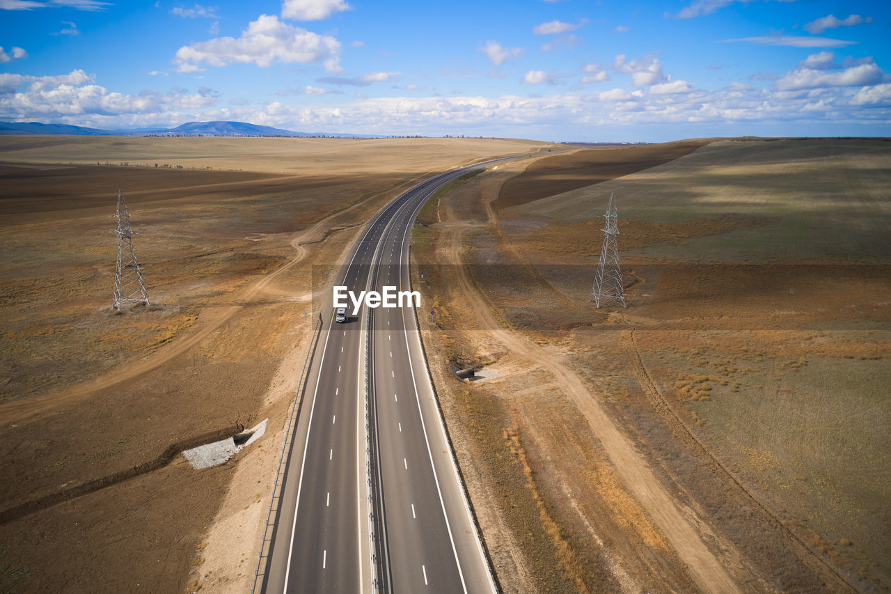 From above drone view of curvy asphalt roadway with lonely car running through desert grassy land in mountainous region in sunny autumn day