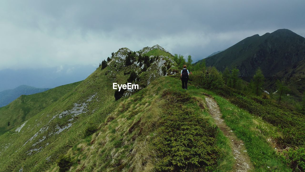 REAR VIEW OF HIKERS WALKING ON MOUNTAIN AGAINST SKY