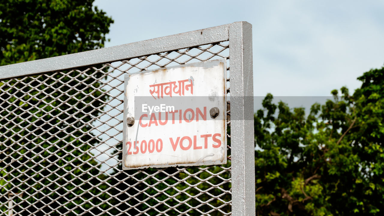 Warning information sign on metal fence against sky