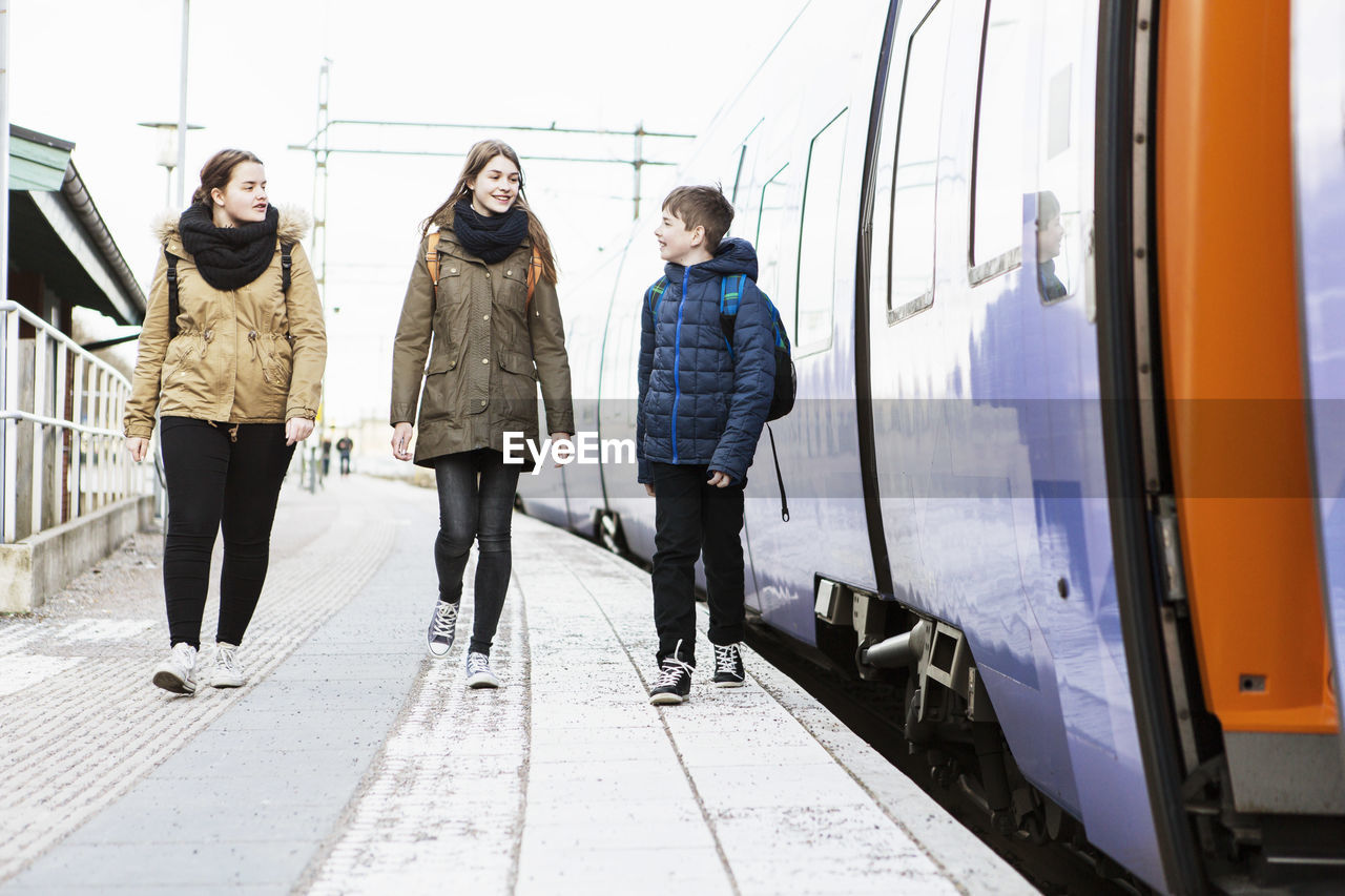 Full length of happy school friends walking on railroad platform