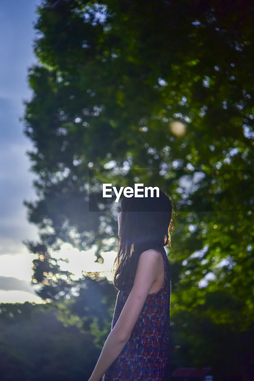 SIDE VIEW OF WOMAN STANDING BY TREE