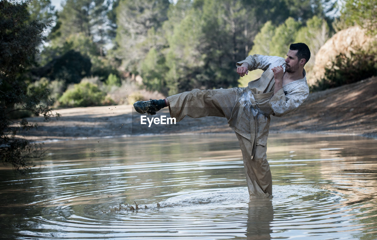 Man kicking in lake against trees