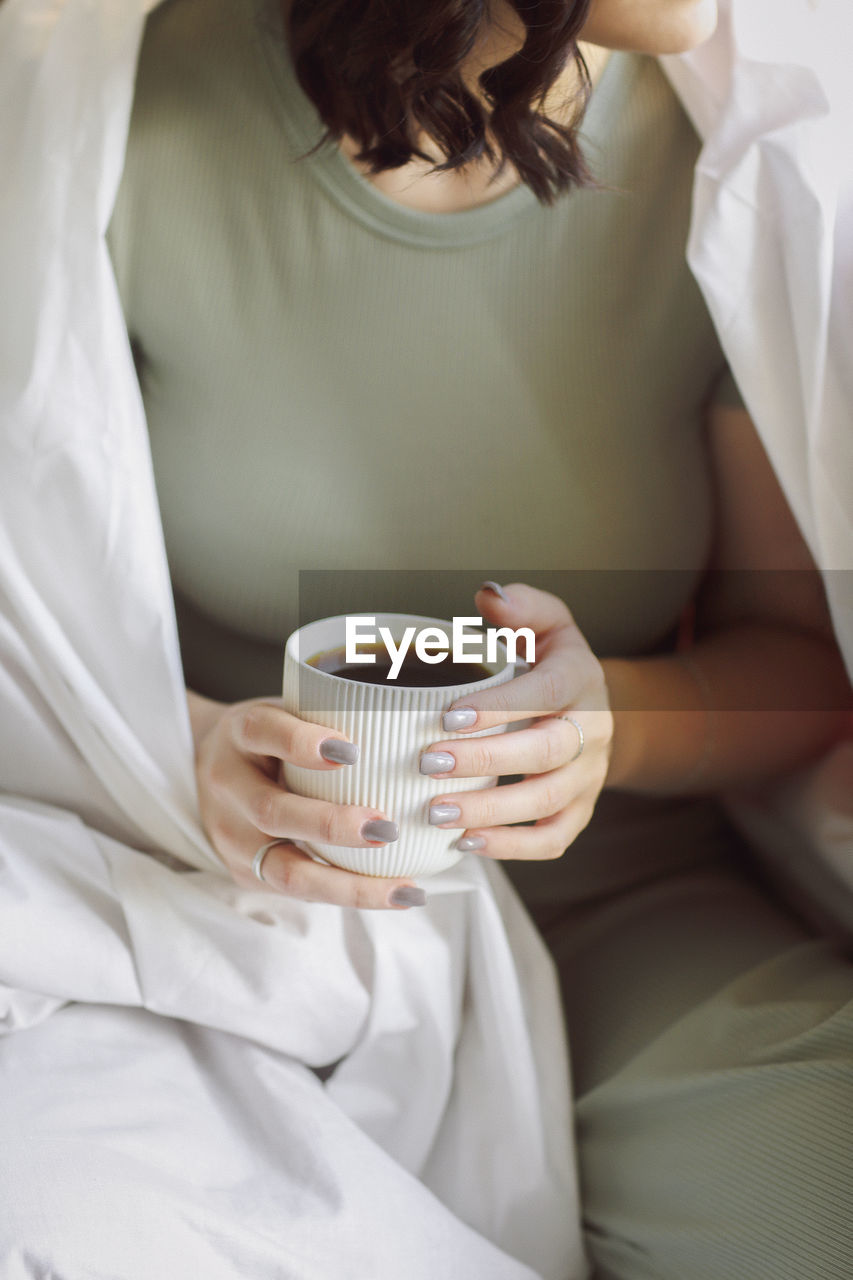 midsection of woman holding coffee cup on bed