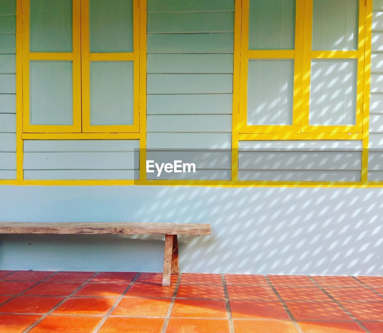 Empty wooden bench against closed windows