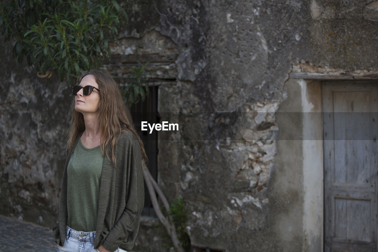 Woman in sunglasses standing against wall