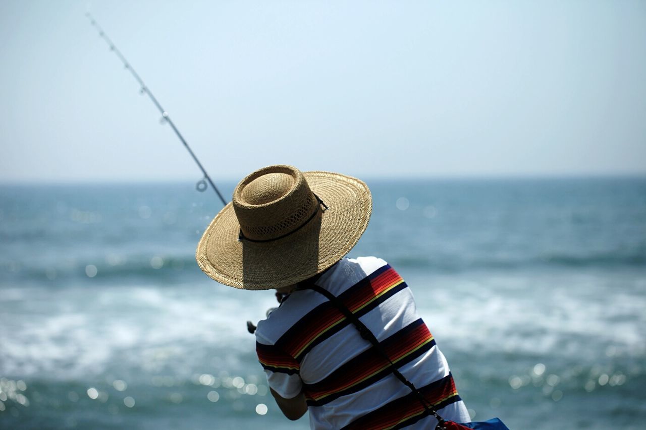 Rear view of man in hat fishing on beach