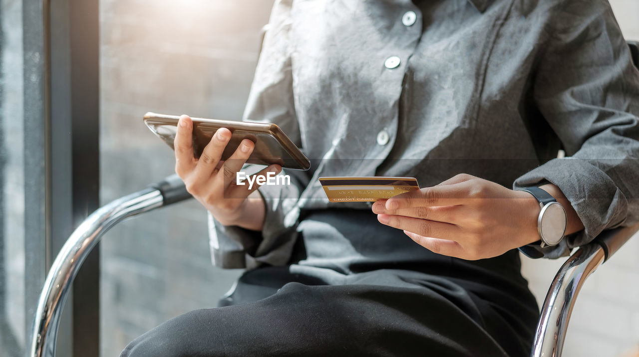 MIDSECTION OF MAN USING MOBILE PHONE IN LAPTOP