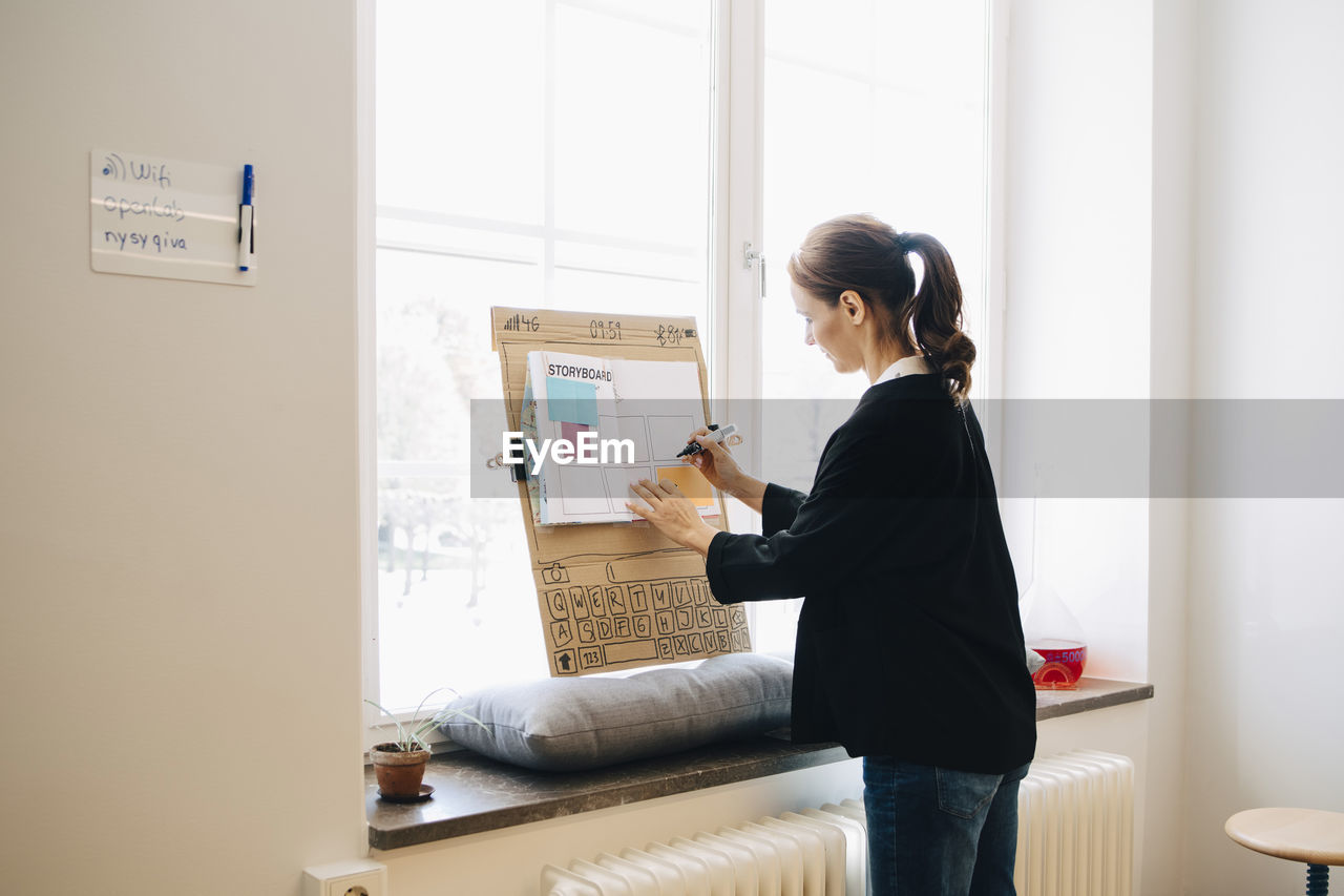 Confident businesswoman writing strategy on placard over window sill at creative office