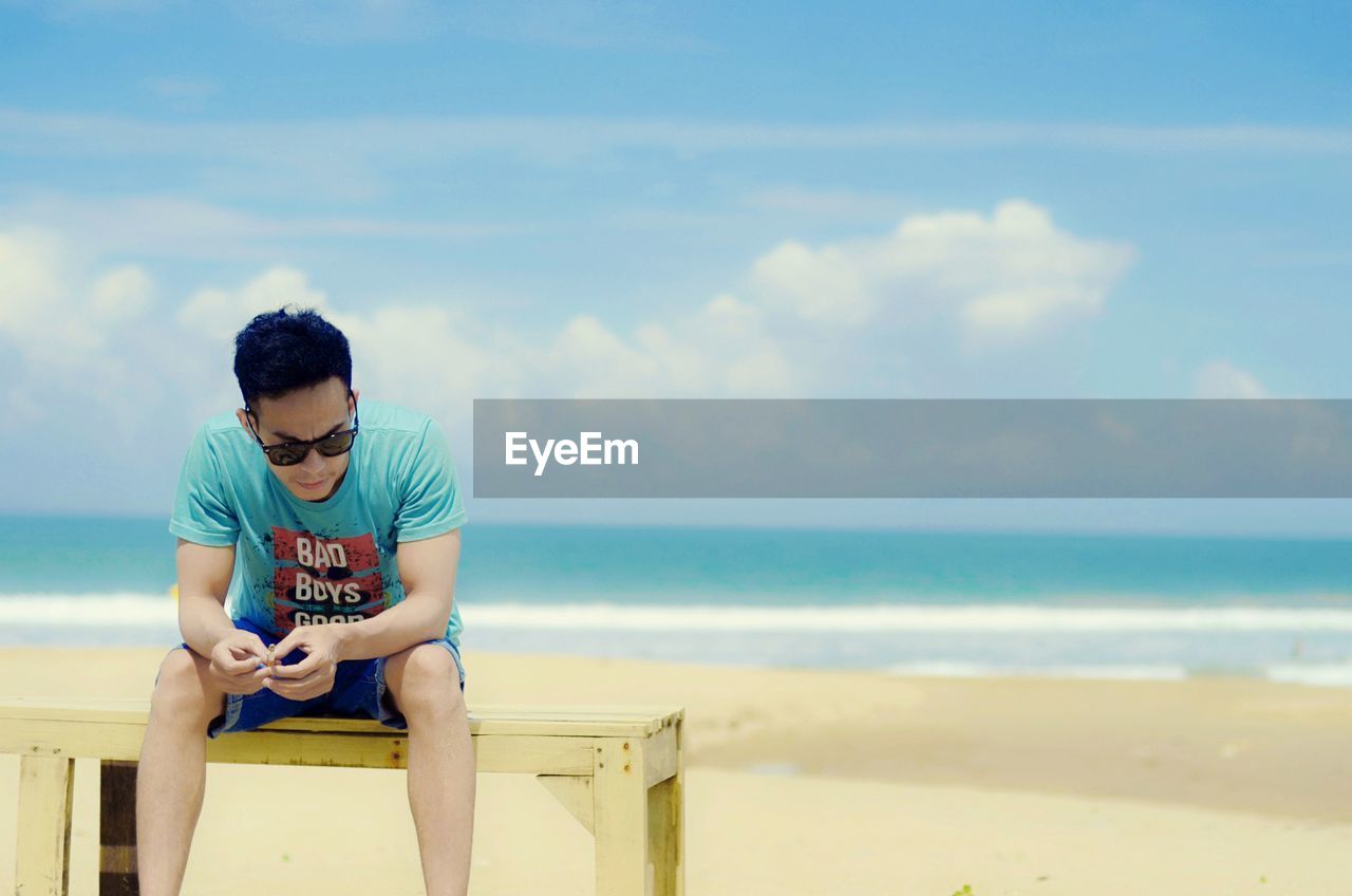 YOUNG MAN SITTING AT BEACH