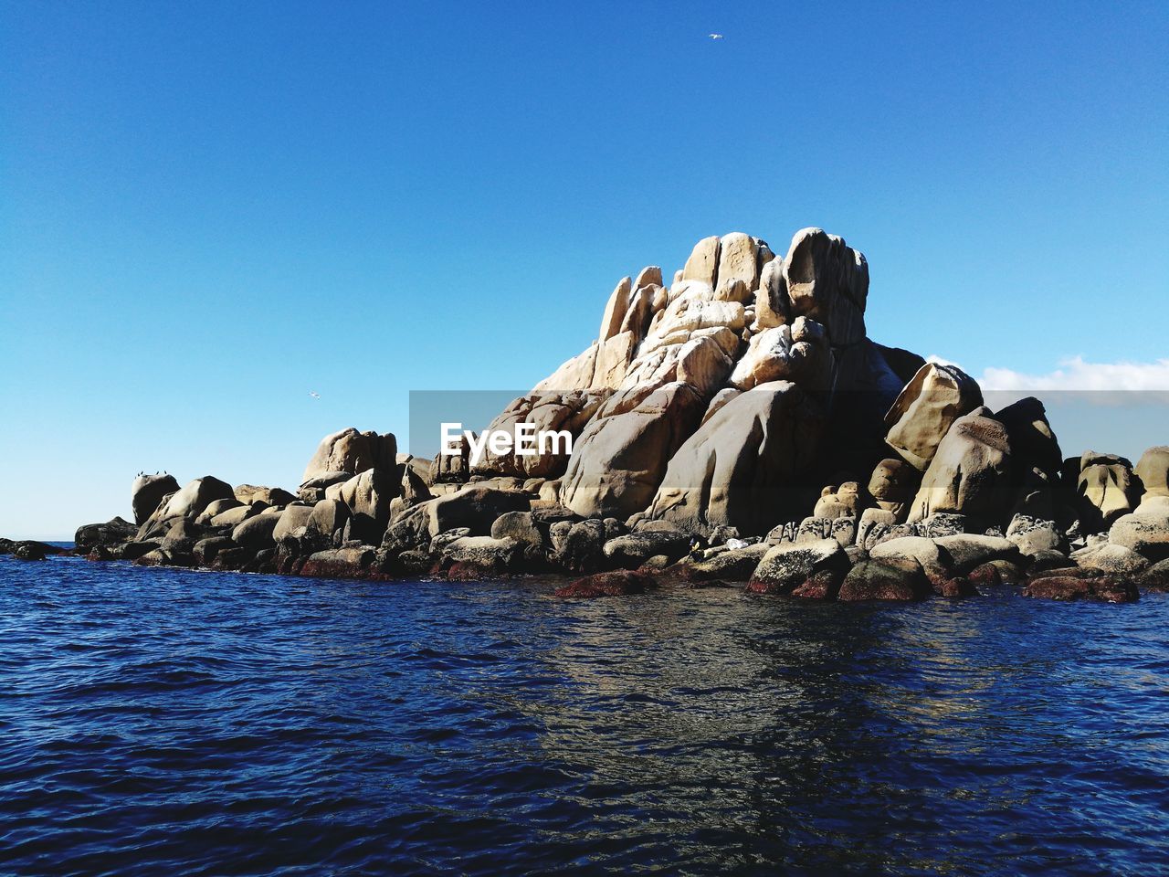 Rock formation in sea against clear blue sky