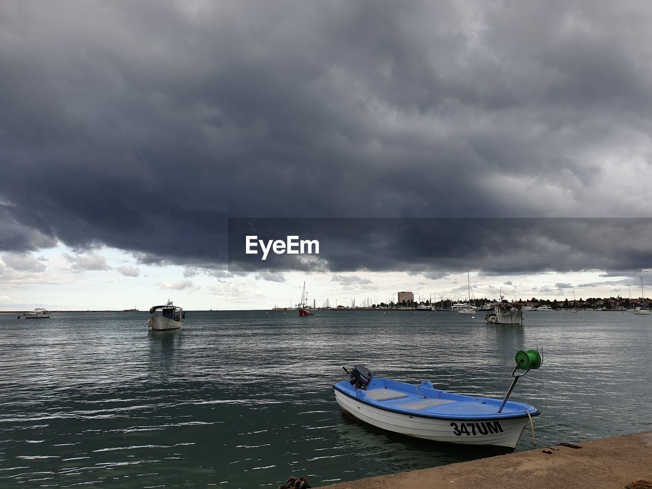 BOATS MOORED ON SEA AGAINST STORM CLOUDS
