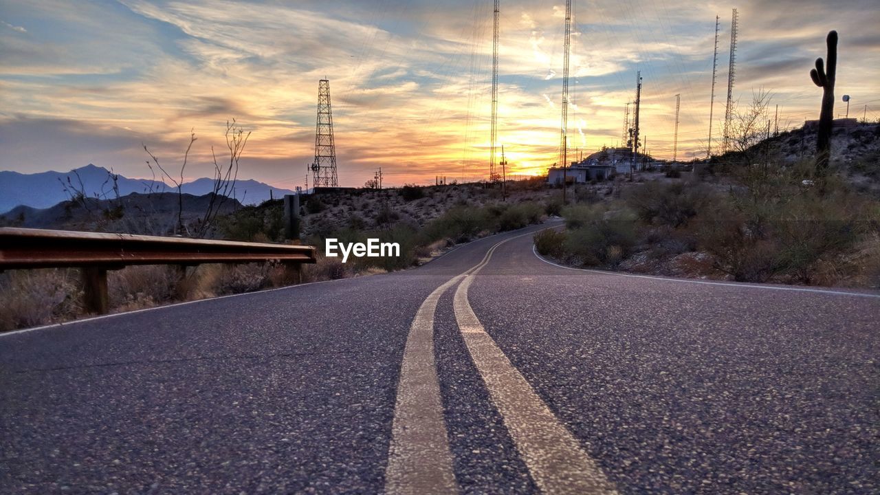 ROAD AMIDST ELECTRICITY PYLON AGAINST SKY DURING SUNSET