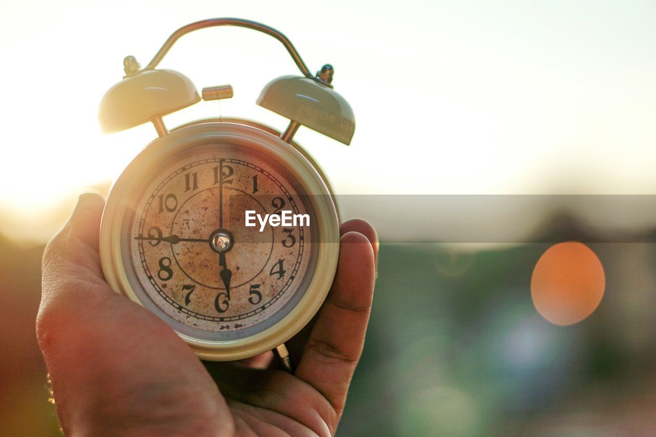 Close-up of hand holding alarm clock against clear sky