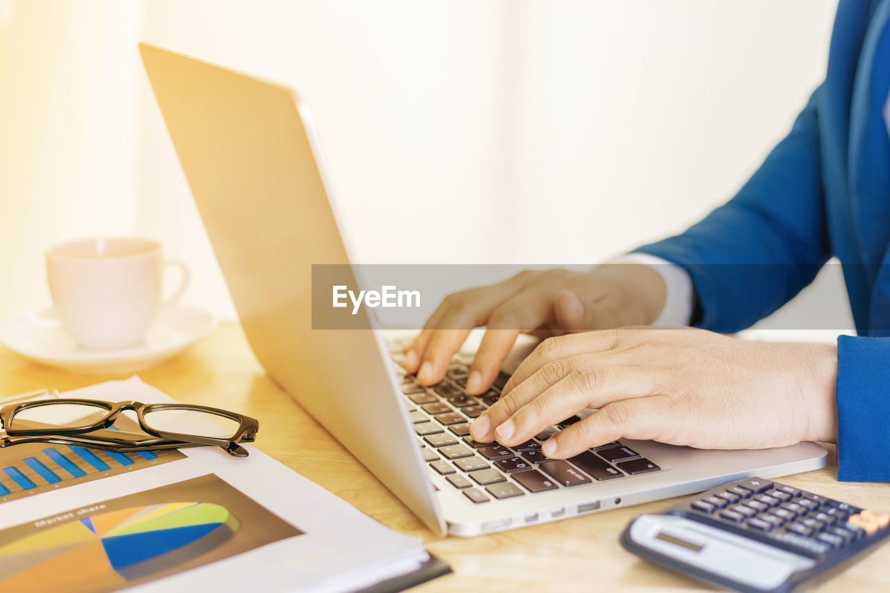 Midsection of businessman using laptop at desk