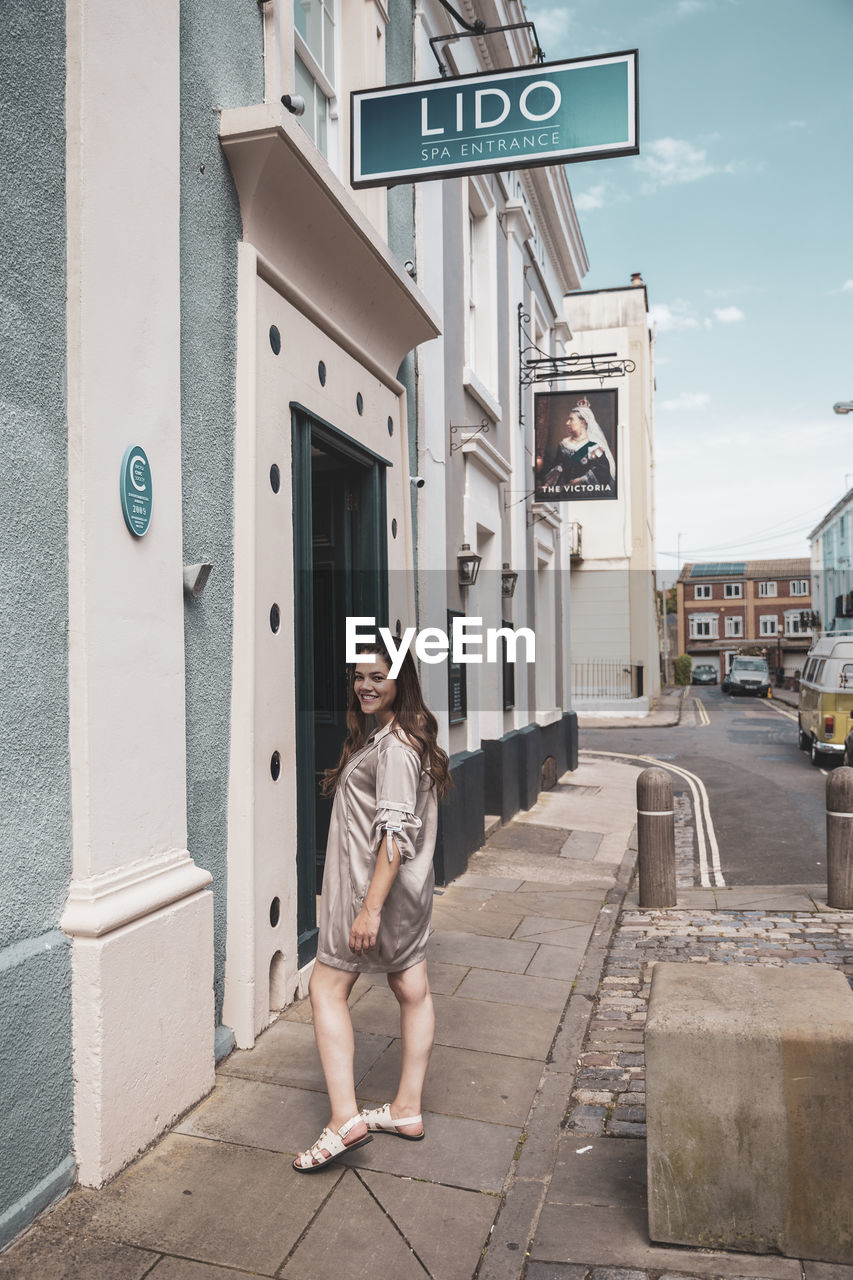 FULL LENGTH PORTRAIT OF YOUNG WOMAN AGAINST BUILDING