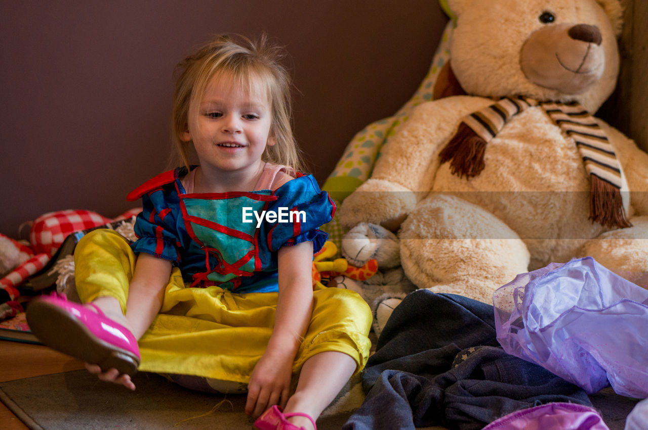 Happy cute girl sitting by stuffed toy at home