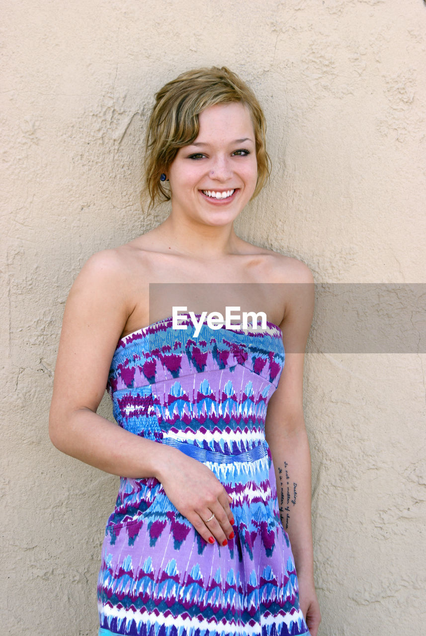 Portrait of smiling young woman standing against wall