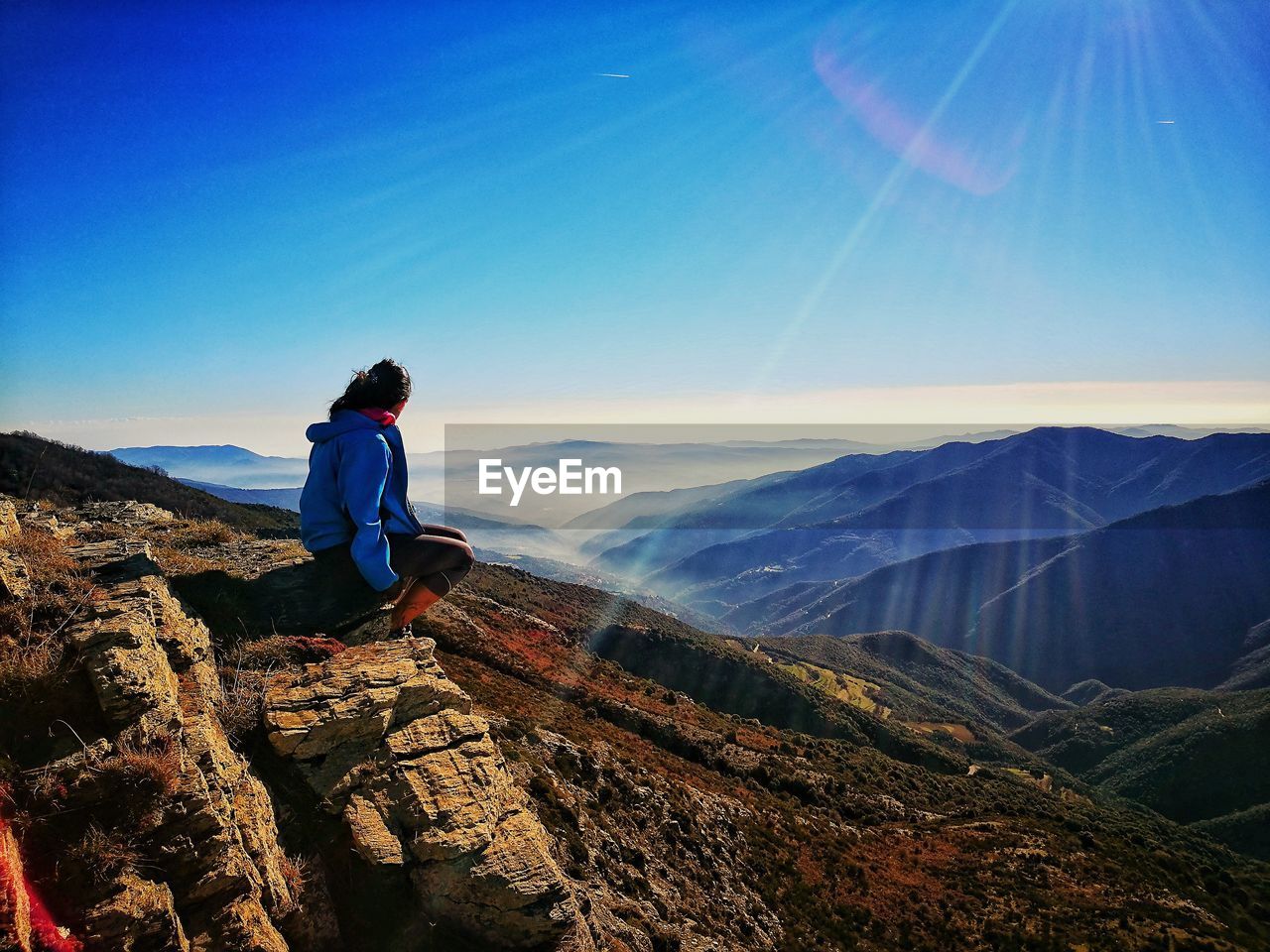 Woman looking away while sitting on mountain against blue sky