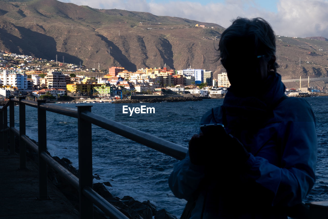 Woman using phone while standing against sea