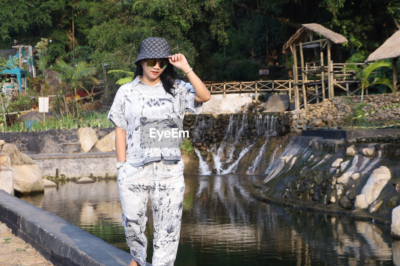FULL LENGTH OF WOMAN STANDING BY LAKE AGAINST BUILT STRUCTURE
