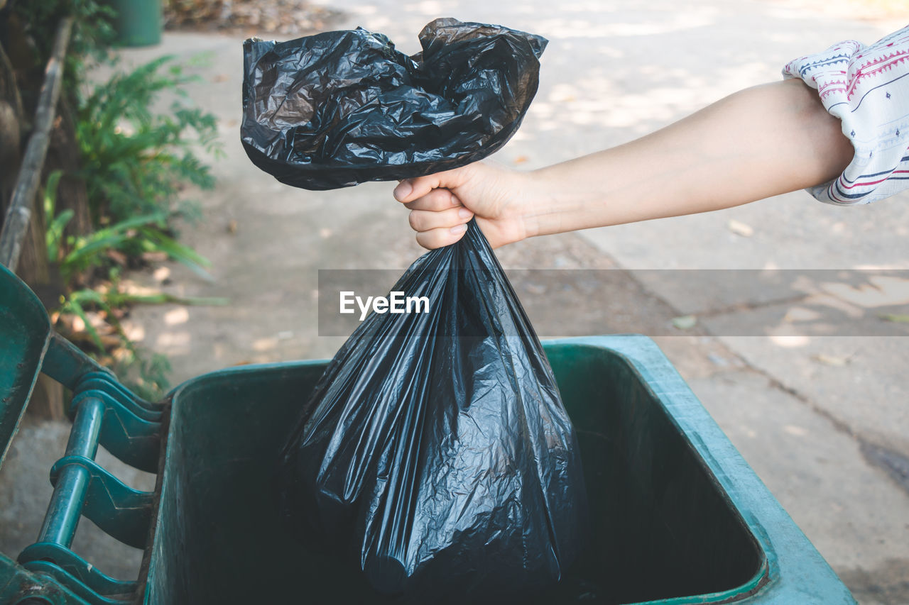 Cropped hand of woman putting plastic bag in dustbin