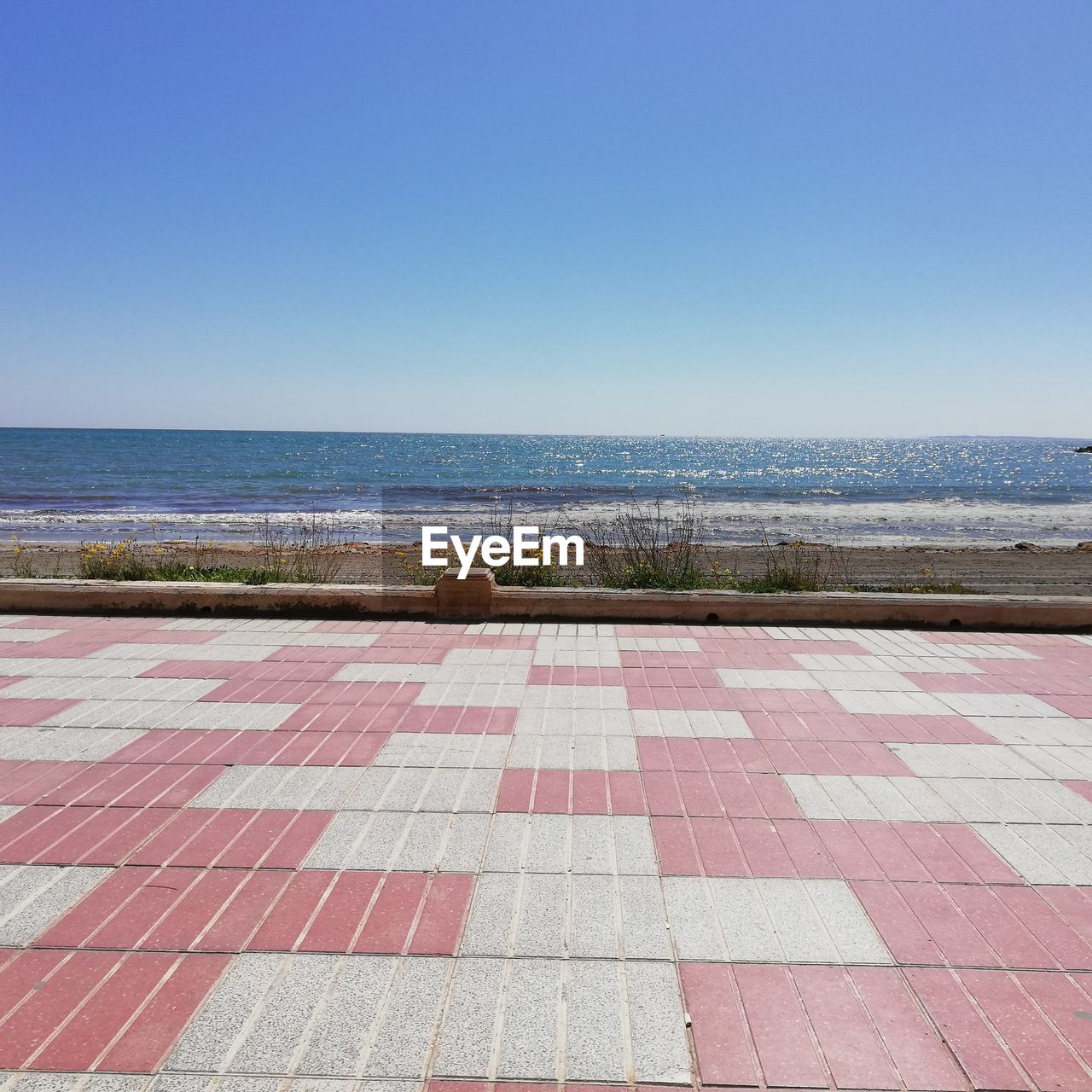 Footpath by sea against clear blue sky