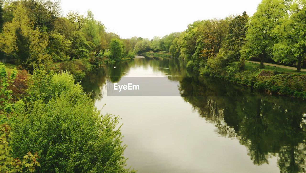 Scenic view of river amidst trees against white sky