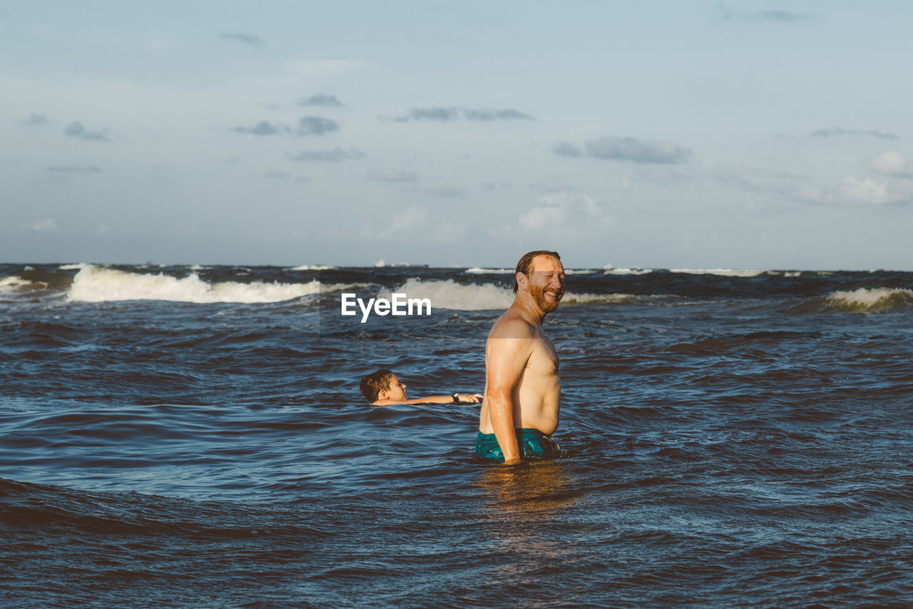 Father and son swimming in sea against sky