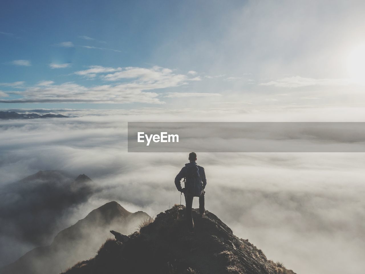 Rear view of young man with backpack standing on mountain against cloudy sky