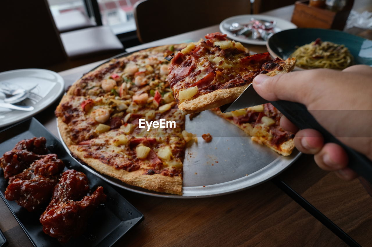 Midsection of person holding pizza in plate on table