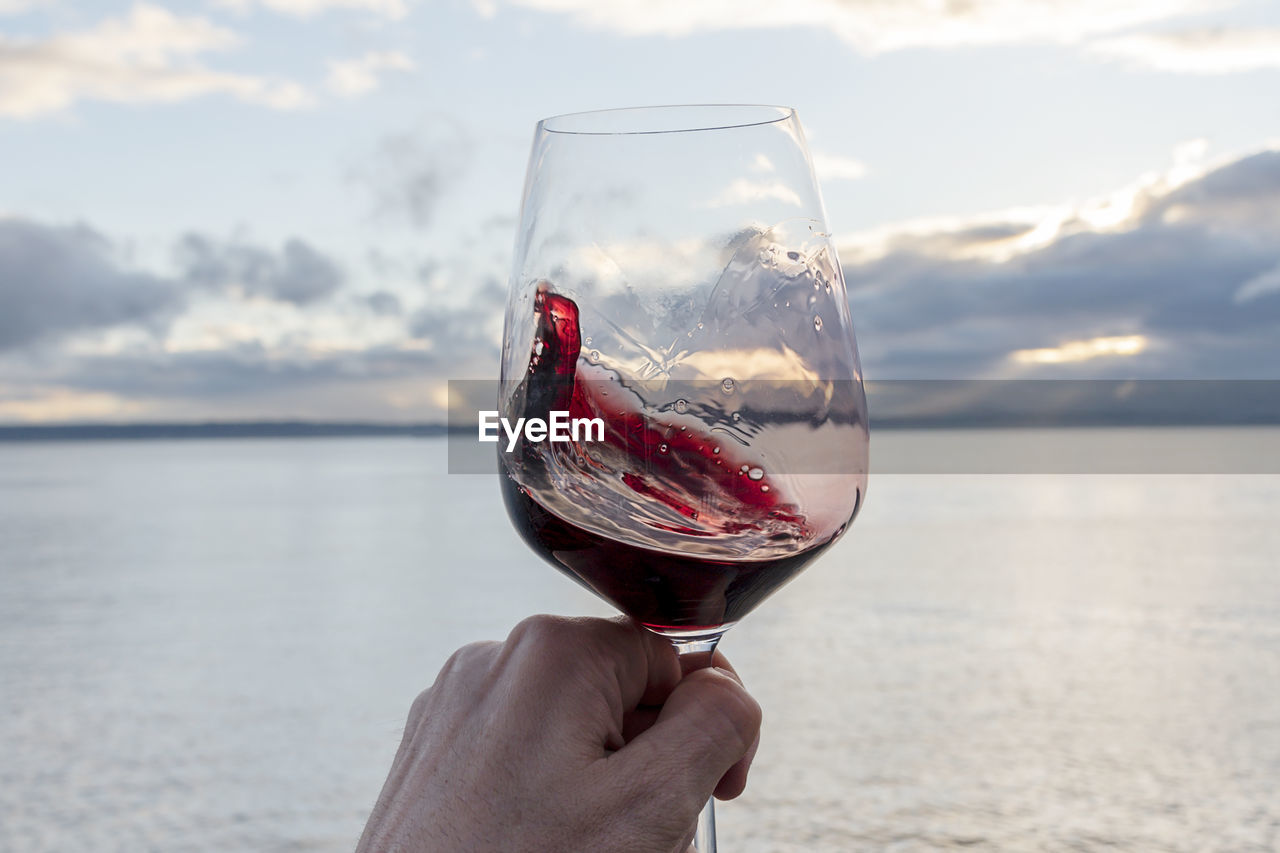 Swirling red wine point of view over sea with dramatic sunset sky.