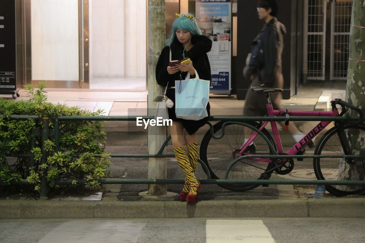 FULL LENGTH OF WOMAN WITH BICYCLE STANDING ON CITY