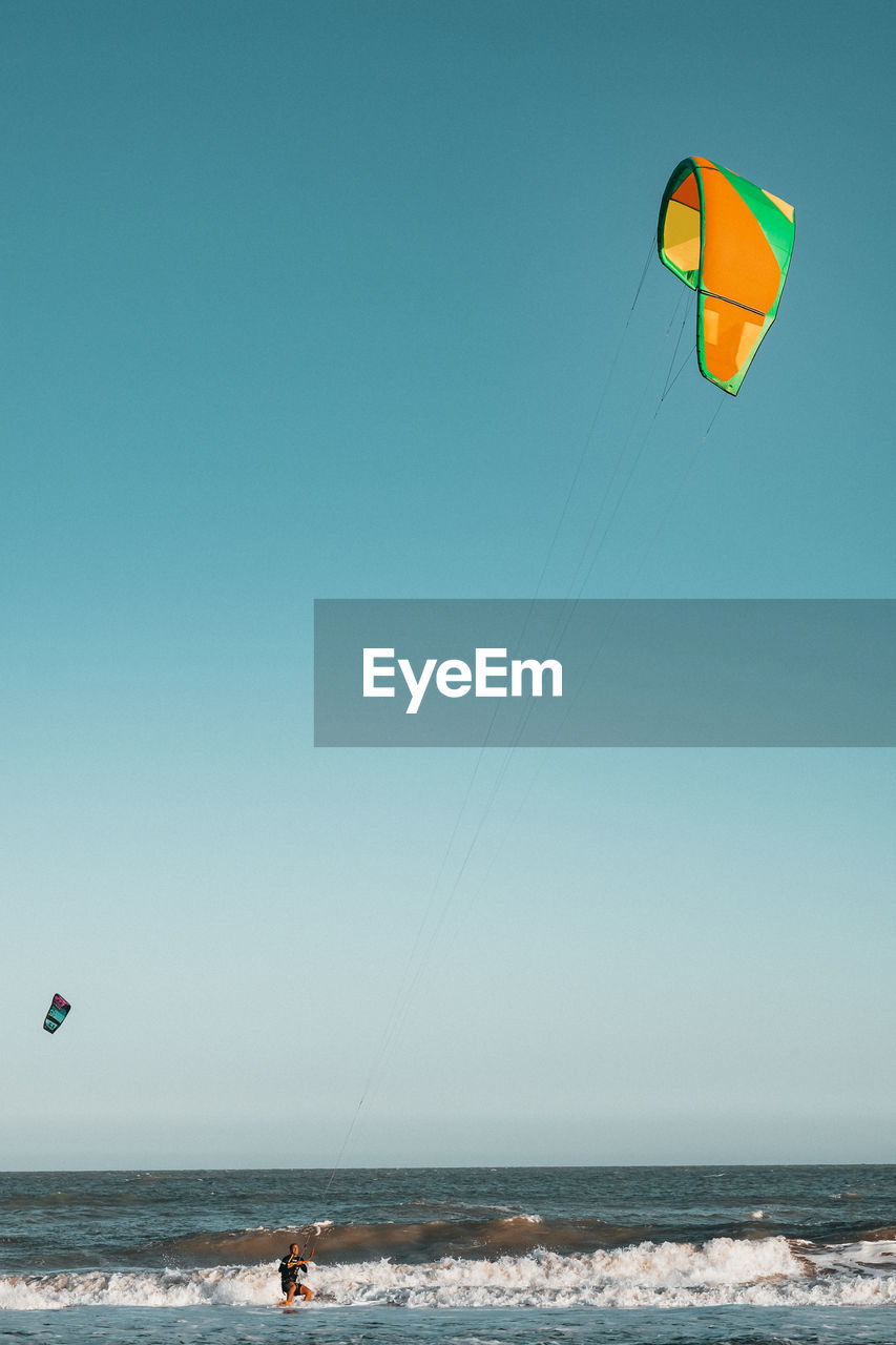 Man kiteboarding on sea against clear sky