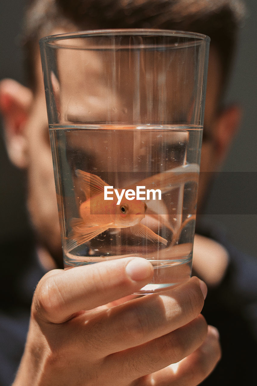 CLOSE-UP OF HAND HOLDING FISH IN GLASS