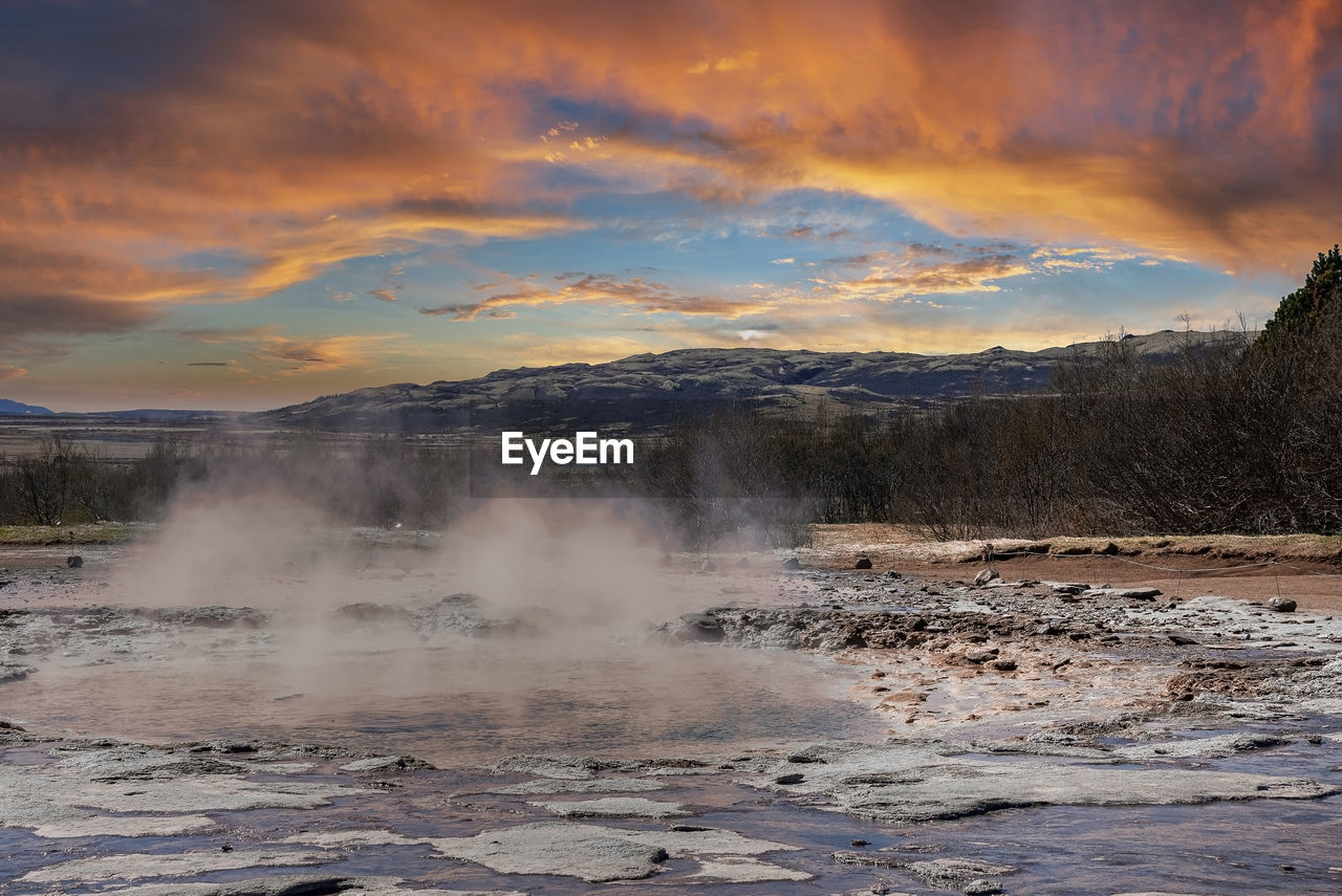 Smoke emitting from geothermal field at smidur geyser valley against cloudy sky